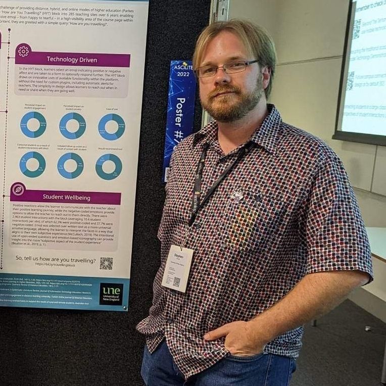 Stephen Grono at a professional event with a PowerPoint presentation and informational banner in the background. 