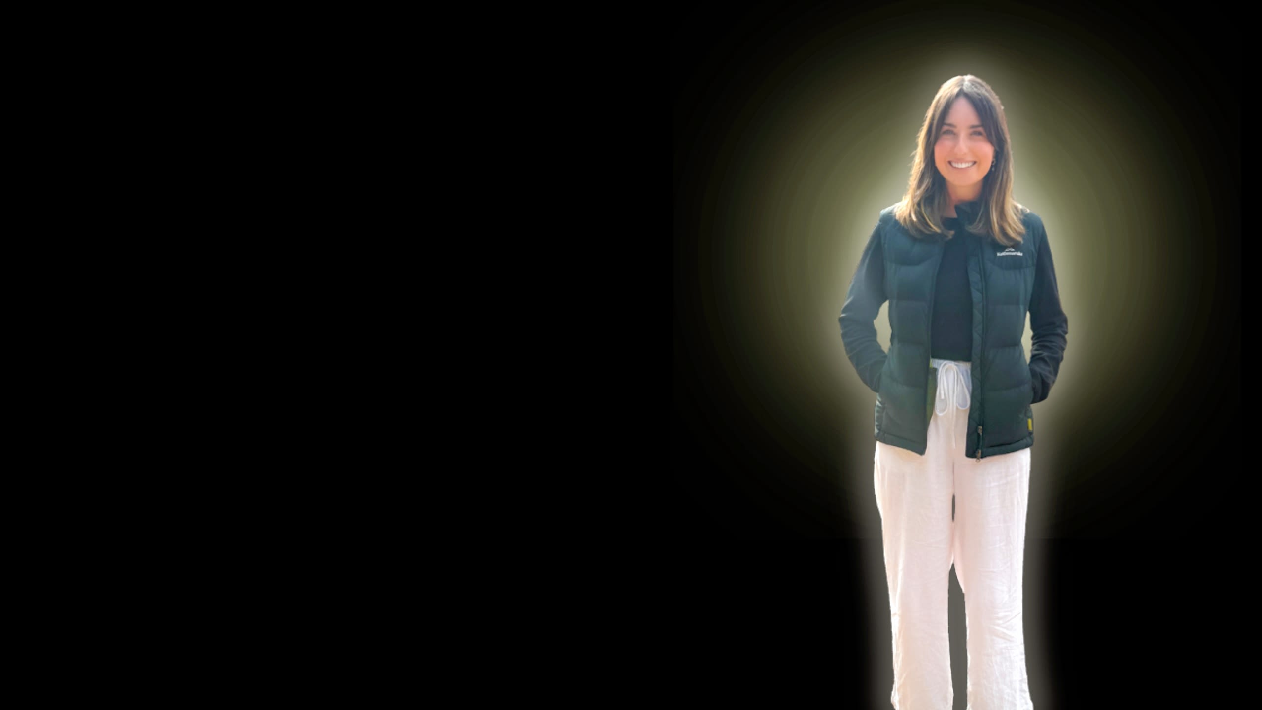 Young woman smiling for photo with hand in her pockets.