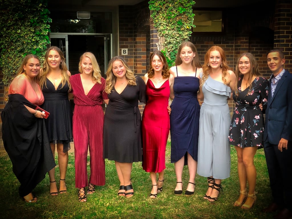 Group of young college students in formal attire pose for a group photo outside.