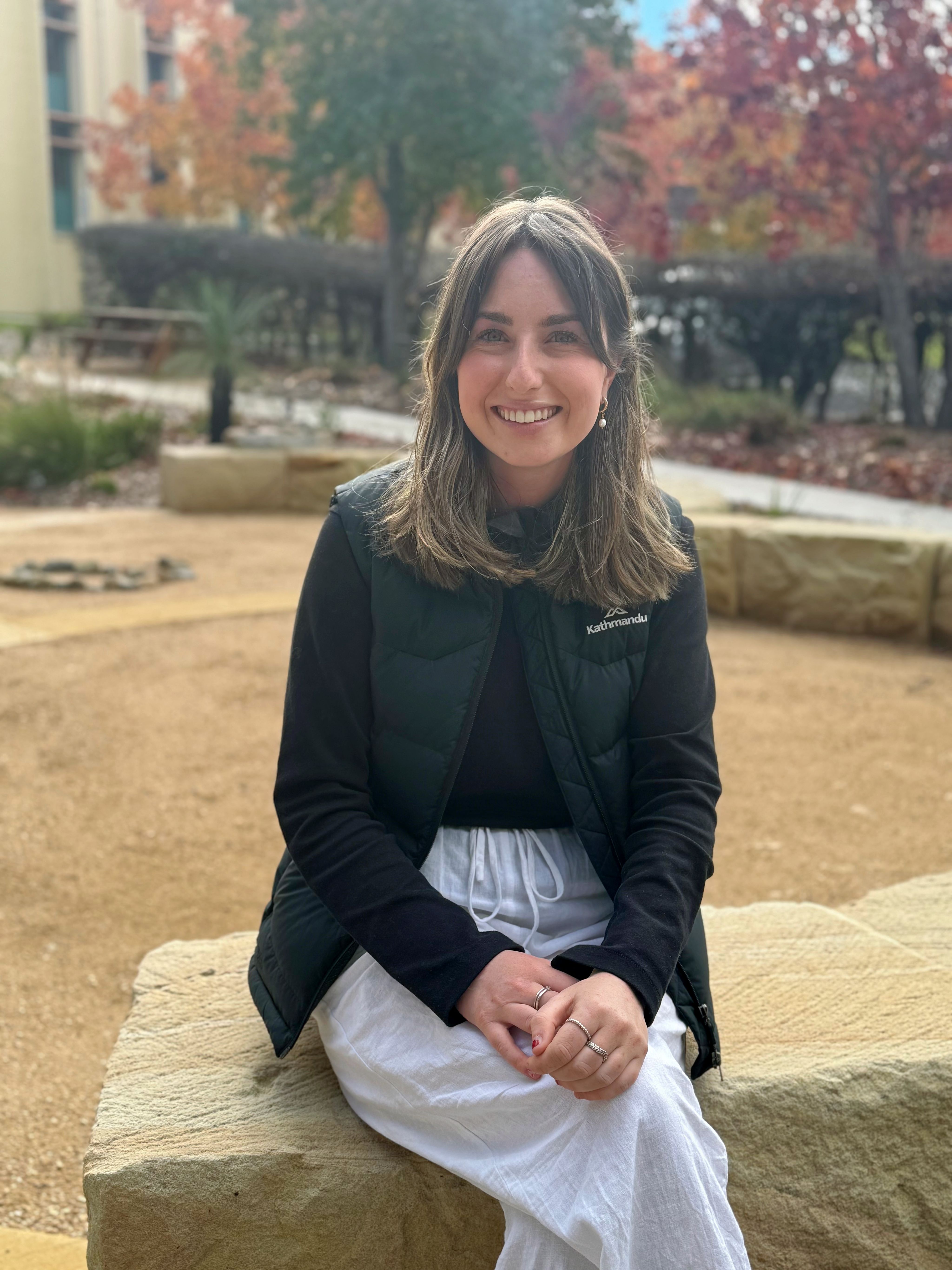 Young woman smiling for photo sitting on a stone bench outside. 