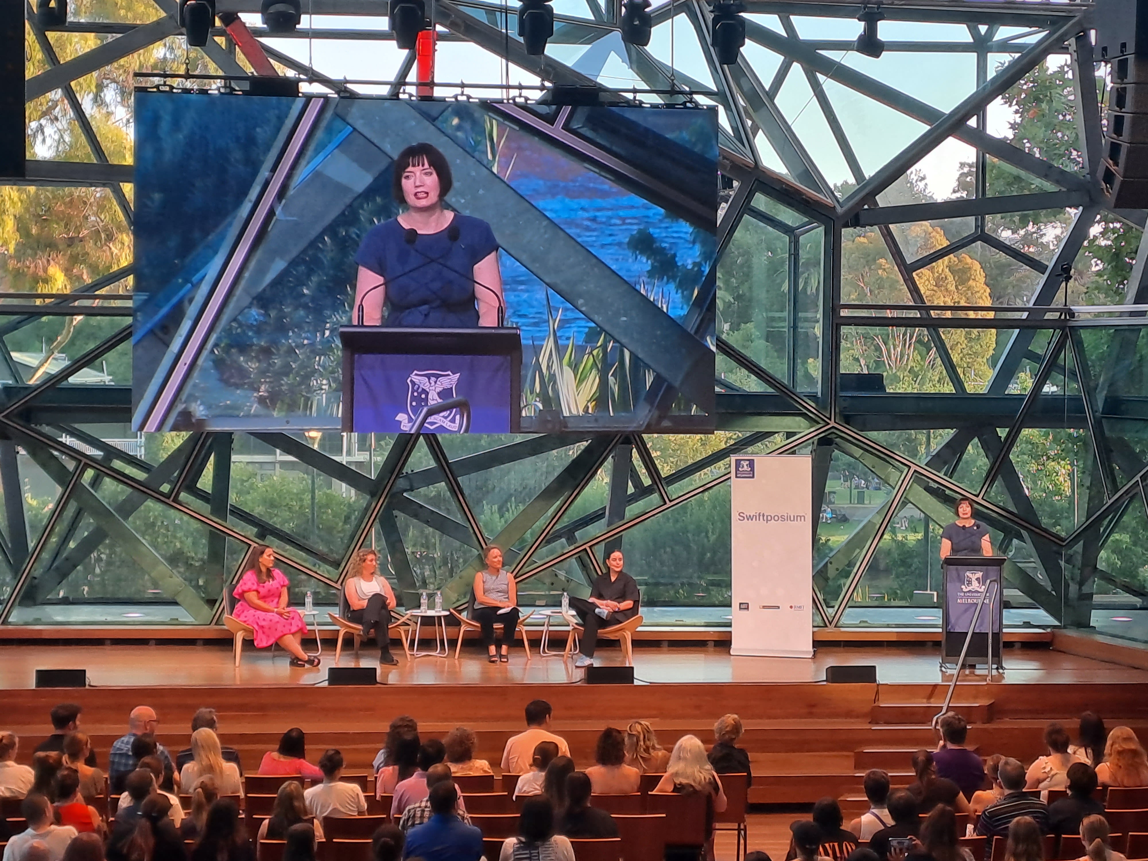 A panel presents on stage inside a large auditorium.